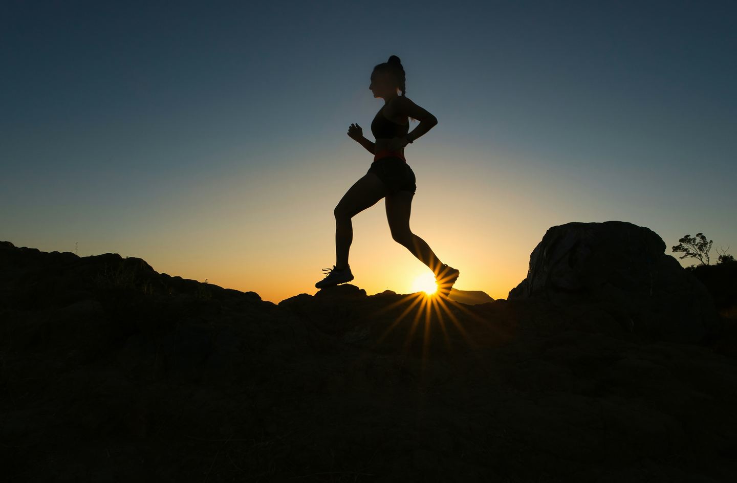 Silhouette einer laufenden Person auf einem Felsgrat bei Sonnenaufgang