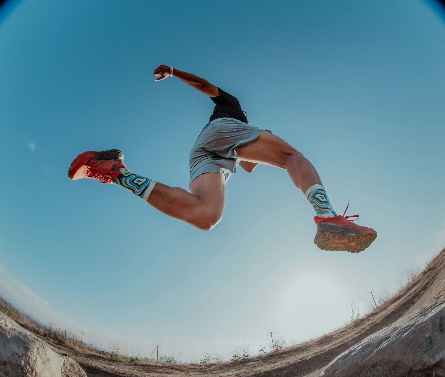A runner leaping over a gully against a blue sky