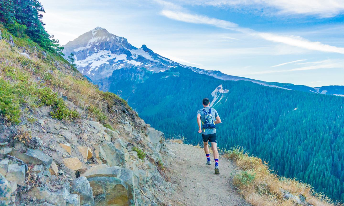 A trail runner on a mountain path facing a glaciated summit