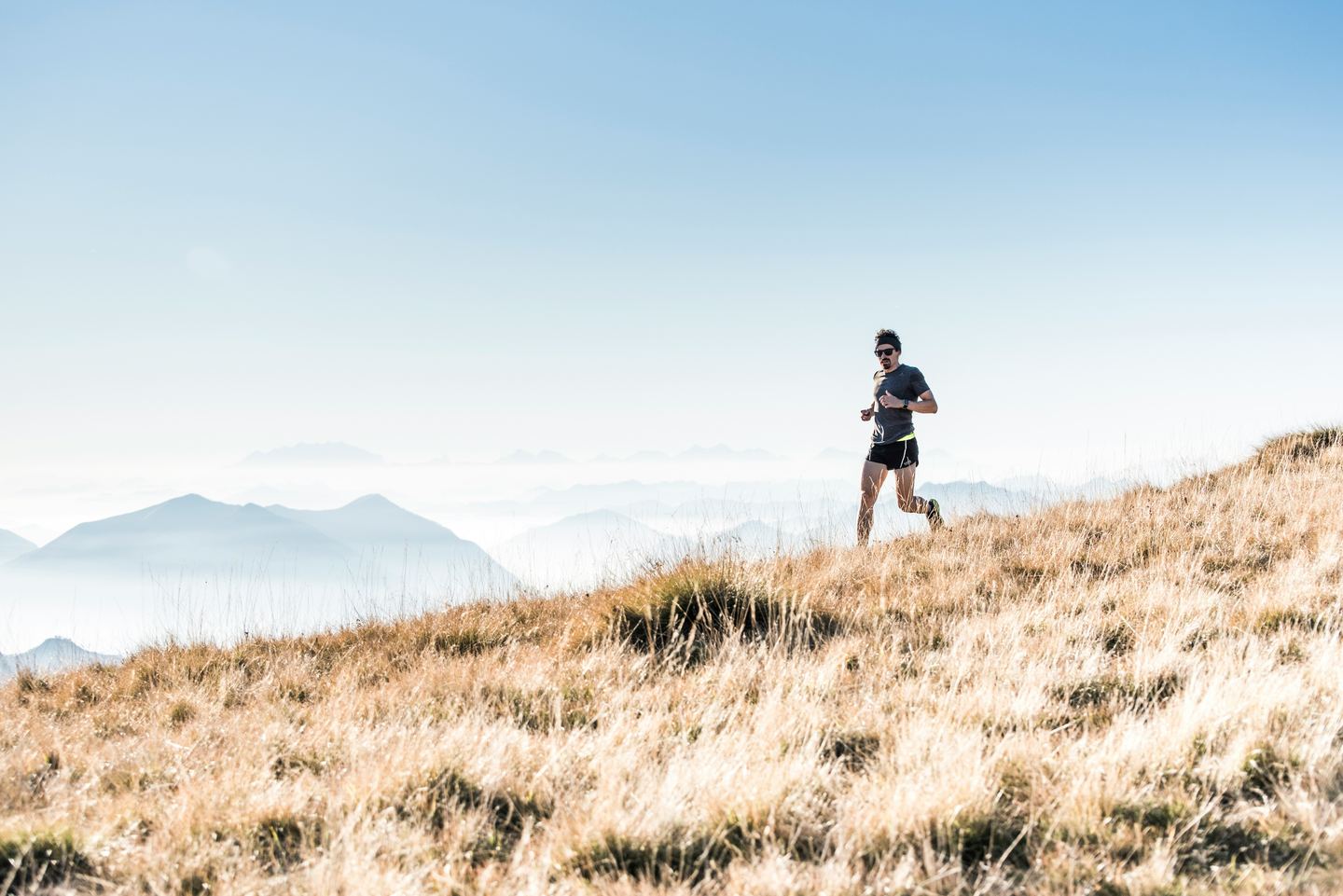 A trail runner on a grassy ridge above a sea of clouds